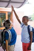 Playful classmates giving high-five at corridor