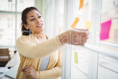 Thoughtful young businesswoman looking at adhesive notes in crea
