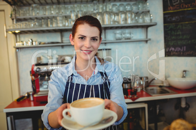 Portrait of happy barista offering coffee at cafe