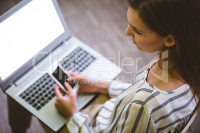 High angle view of businesswoman using cellphone over laptop at