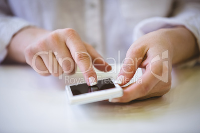 Close-up of businesswoman touching cellphone on desk at office