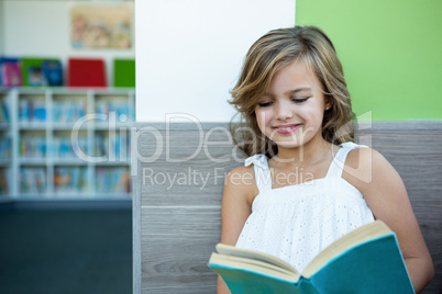 Smiling girl reading book in school library