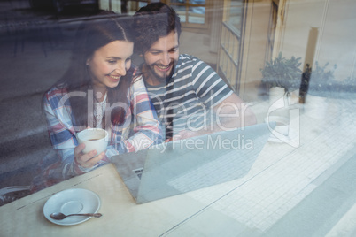 Happy couple using laptop at cafe