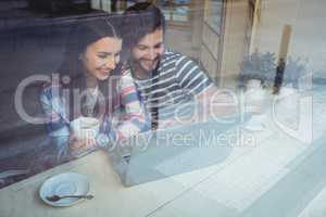 Happy couple using laptop at cafe