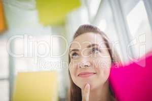 Thoughtful businesswoman looking at adhesive notes on window in