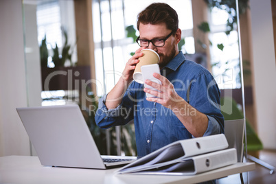 Businessman drinking office while using cellphone at creative of