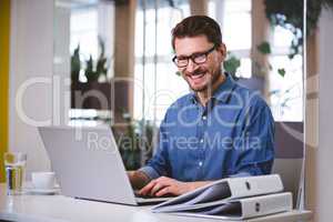 Portrait of cheerful businessman working on laptop at creative o