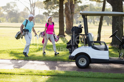 Full length of mature golfer couple by golf buggy