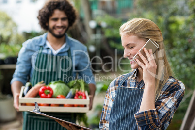 Female gardener talking on cellphone while man in background