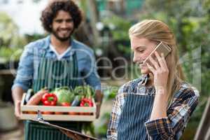 Female gardener talking on cellphone while man in background