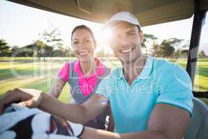 Confident golfer couple sitting in golf bugggy