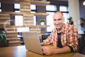 Happy businessman using laptop at desk in creative office