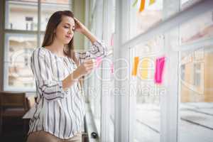 Thoughtful businesswoman holding adhesive note by window in crea
