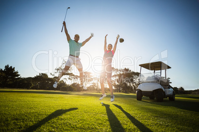 Full length of golf player couple with arms raised