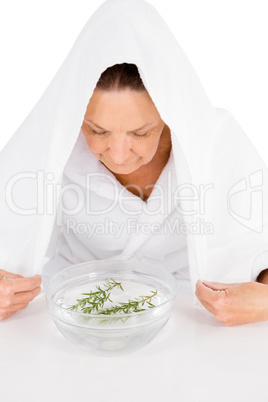 Mature woman steaming face with rosemary in bowl of water