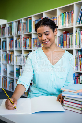 Happy young woman writing on notebook in library