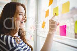 Happy businesswoman touching adhesive notes on window in creativ