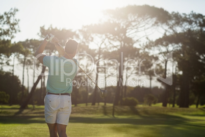 Rear view of young golfer taking shot