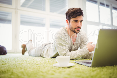 Businessman lying on carpet while using laptop in office
