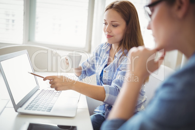 Businesswoman pointing on laptop with colleague in office