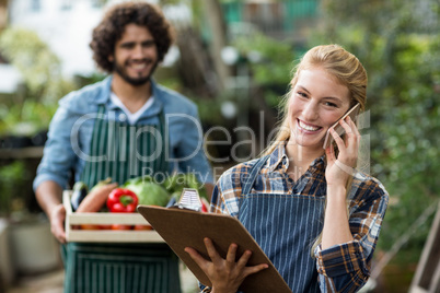 Female gardener talking on mobile phone while man standing