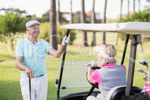 Mature man looking at woman sitting in golf buggy
