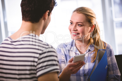 Beautiful executive with cellphone looking at colleague at creat