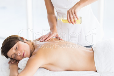 Midsection of masseur pouring oil on woman back