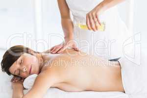 Midsection of masseur pouring oil on woman back