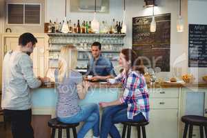 Waiter looking at female customers sitting at counter in cafe