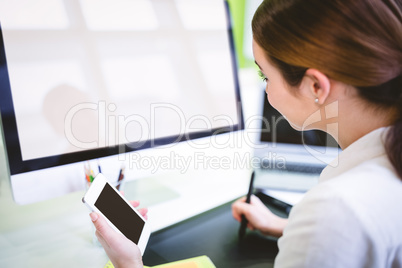 Graphic designer holding phone while working at desk