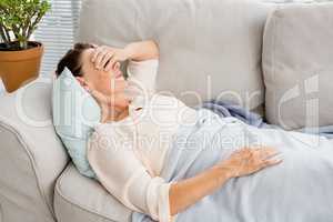 Mature woman having headache while lying on sofa