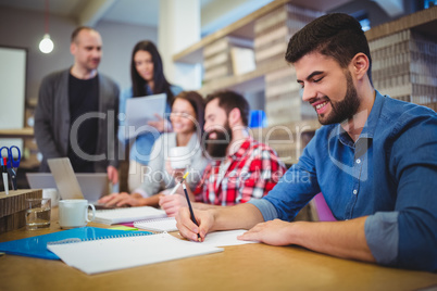 Businessman writing on paper while colleagues in background