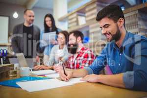 Businessman writing on paper while colleagues in background