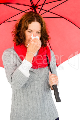 Mature woman suffering from cold while holding umbrella