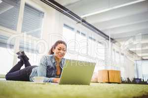 Portrait of businesswoman lying on carpet while using laptop