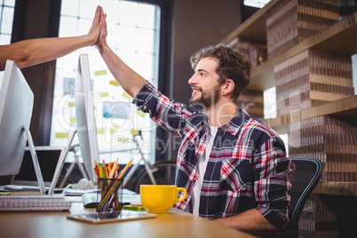 Creative coworkers high fiving at desk in office