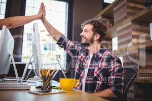 Creative coworkers high fiving at desk in office