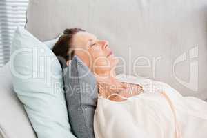 Mature woman listening to music while lying on sofa