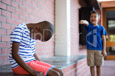 Boy laughing on sad classmate in corridor