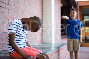 Boy laughing on sad classmate in corridor