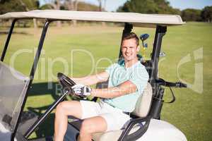 Happy golfer man driving golf buggy