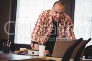 Businessman leaning while using laptop at desk in creative offic