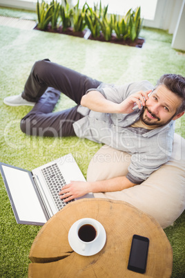 Portrait of happy businessman using laptop and mobile phone at c