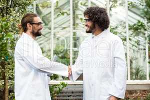Male scientists handshaking outside greenhouse