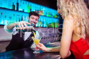 Bartender serving cocktail to young woman at counter