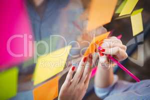 Businesswoman writing on sticky notes stuck to glass