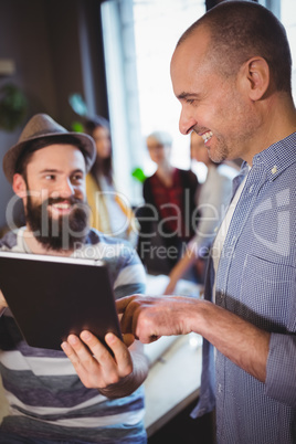 Happy male coworkers discussing over digital tablet