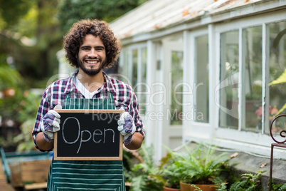 Gardener holding open sign placard outside greenhouse