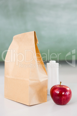 Apple with drink bottle and paper bag on table